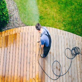 A The Exterior Group technician pressure washing concrete surrounding a pool.