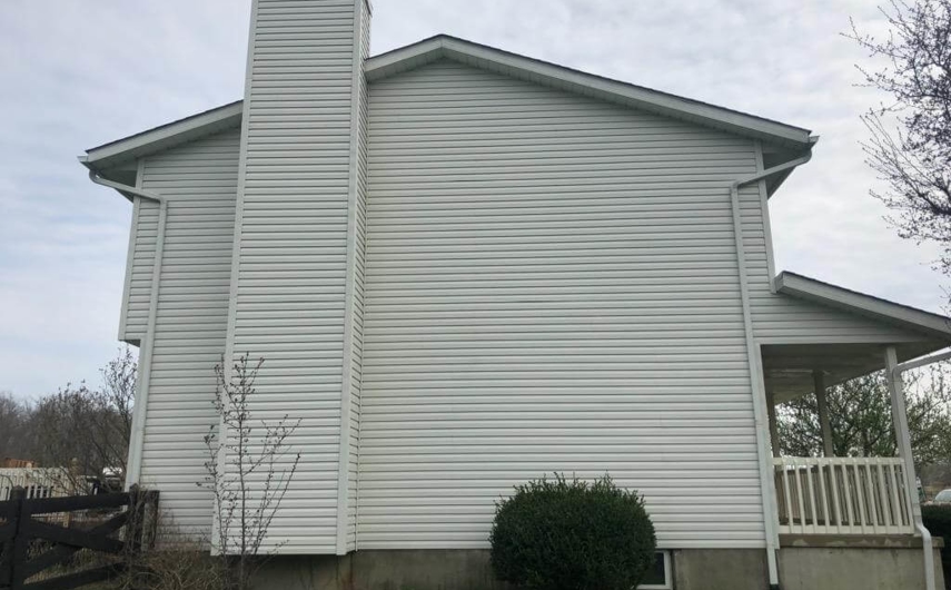 Newly cleaned siding on a white two-story house with a chimney.